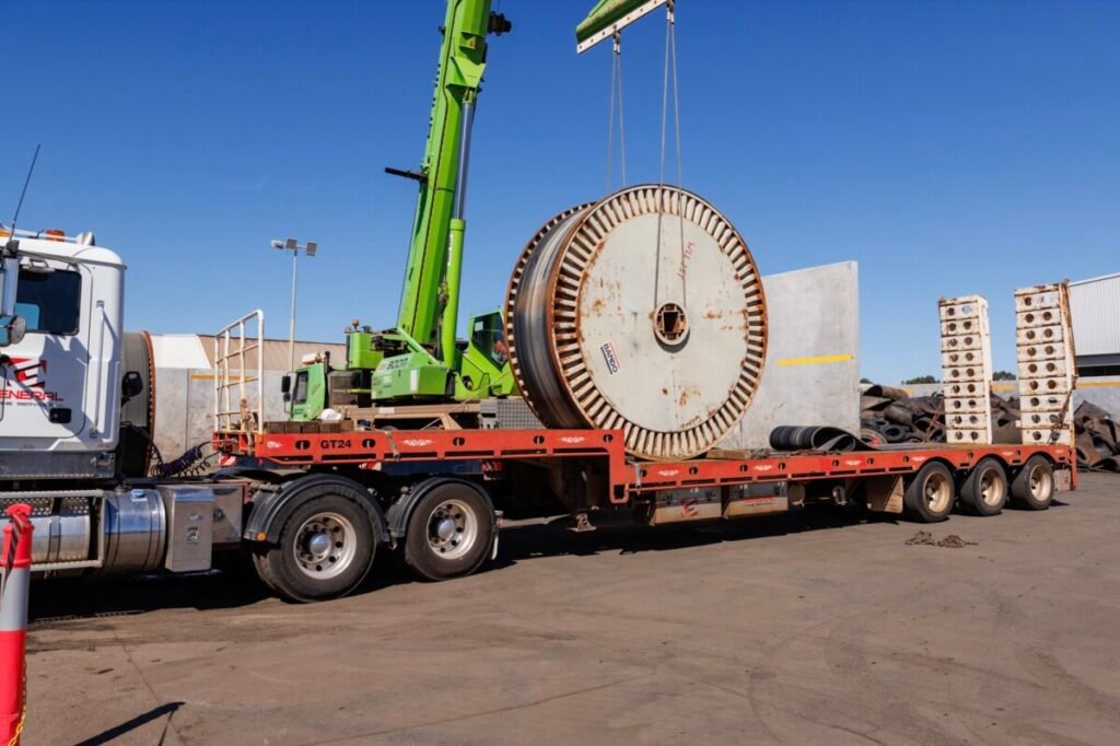 (Image source: Brodie Butler Photography) A crane prepares to unload one of 80 reels of used conveyer belt being sent from Alcoa’s mine sites to Tyrecycle in East Rockingham for recycling.